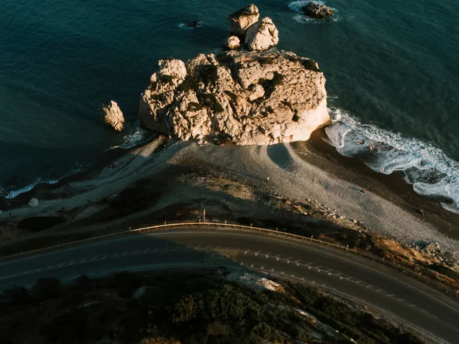 The coast road curving past a rock in the sea in Cyprus, seen from above at sunset.